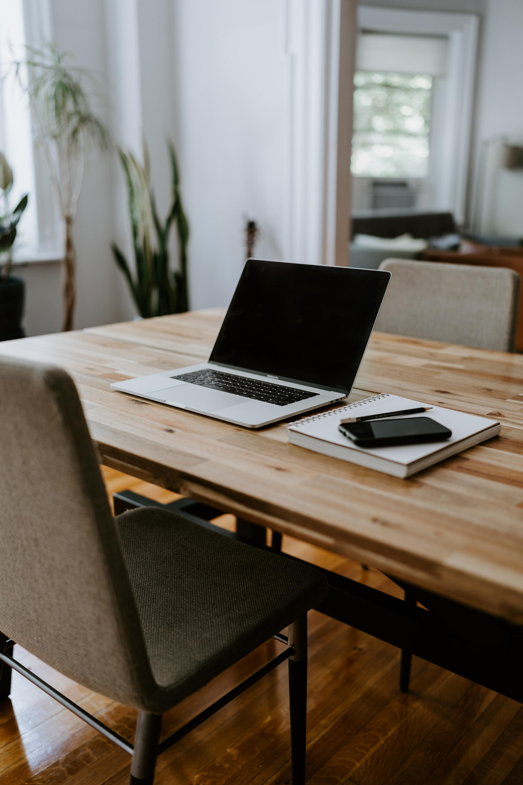 Laptop and notebook on a wooden table with seating in a bright workspace Laptop and notebook on a wooden table with seating in a bright workspace